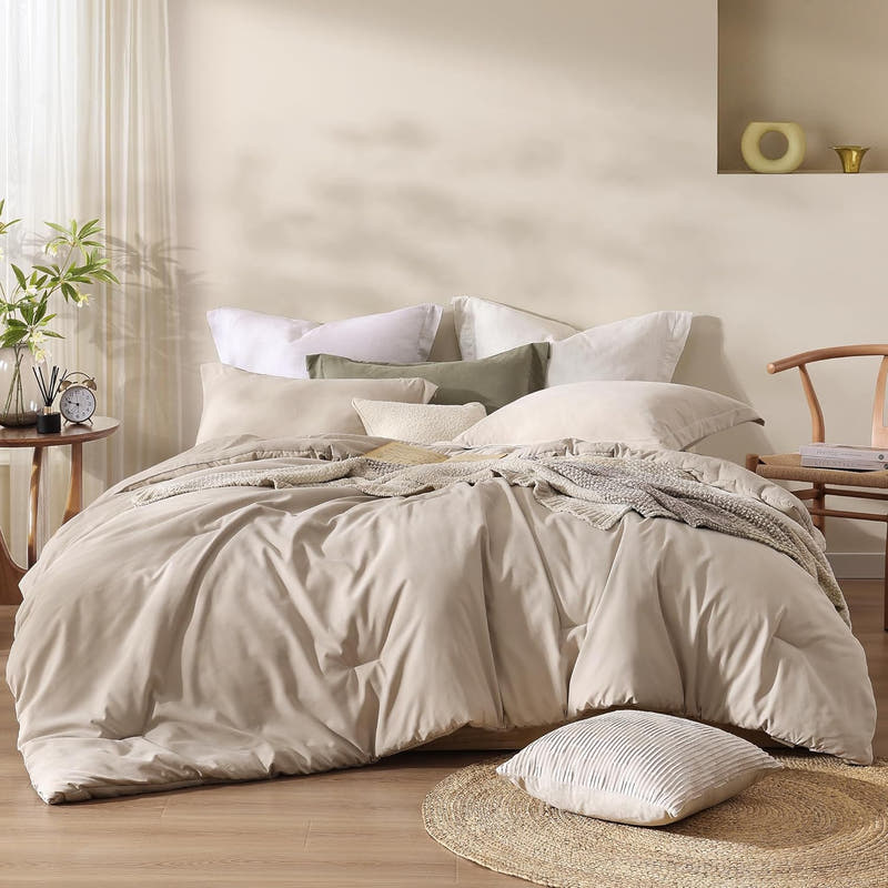 A queen-sized beige comforter set with a microsuede-like texture is displayed on a bed in a room with minimalist decor. The set includes a comforter and two shams.