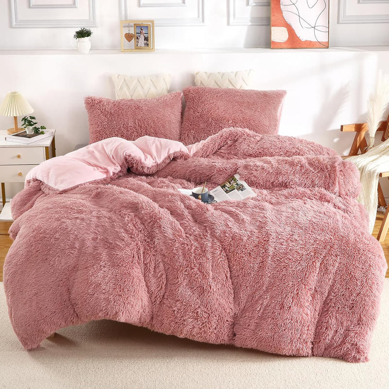 A fluffy pink duvet cover set on a bed, including a duvet cover and two pillow shams, presented in a bright room setting.