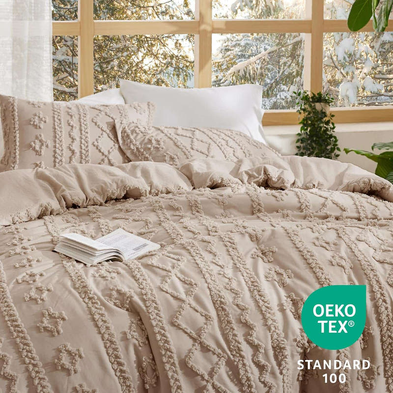 Beige textured bedding set on a bed with a window in the background, featuring OEKO-TEX Standard 100 logo.