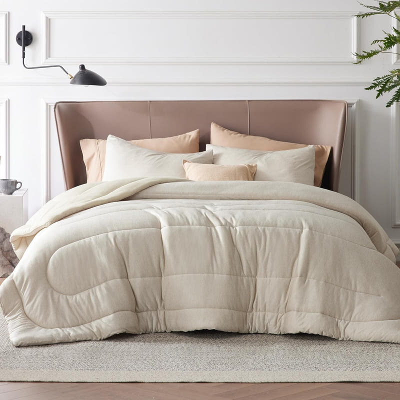 A queen-sized comforter set with a beige color, displayed on a bed with four pillows, in a room with a neutral interior design.